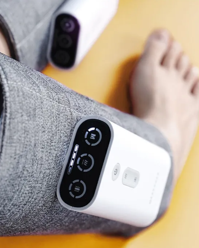 Woman wearing a gray heated leg massager on both legs standing on a yellow floor