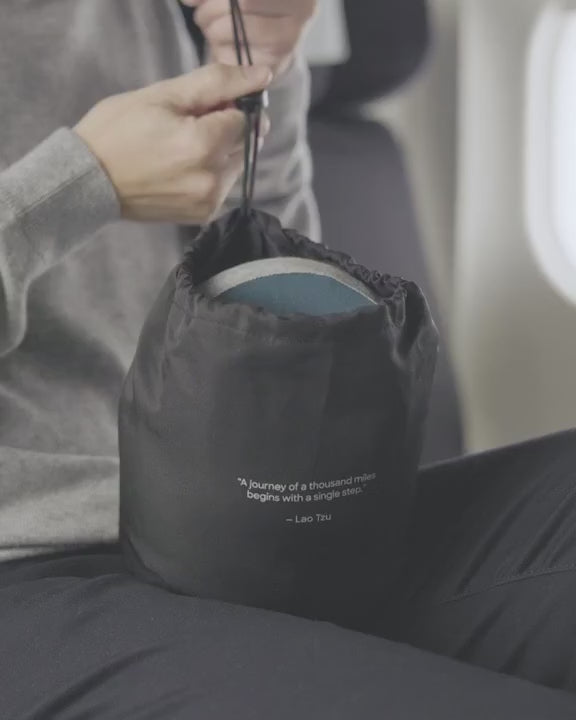 Person putting a gray memory foam neck pillow inside a black sealable bag
