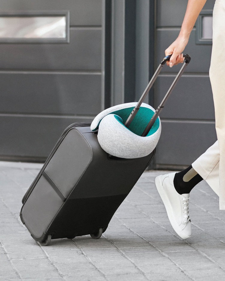 Person pulling her baggage with a gray memory foam neck pillow fastened around it