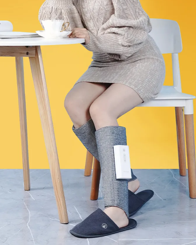 Women sitting at a table, drinking coffee and wearing a gray heated leg massager on both legs