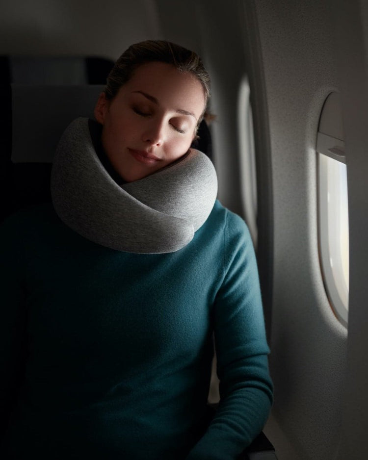 Woman sleeping on an airplane while wearing a gray memory foam neck pillow